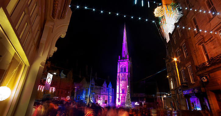 View of crowds and buildings light up in different colours during Durham Christmas Festival during night time.